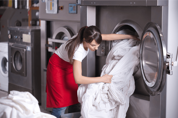 Woman in red apron washing linens at industrial washing machine