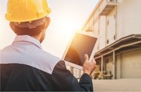 Person wearing yellow construction helment holding tablet at building site