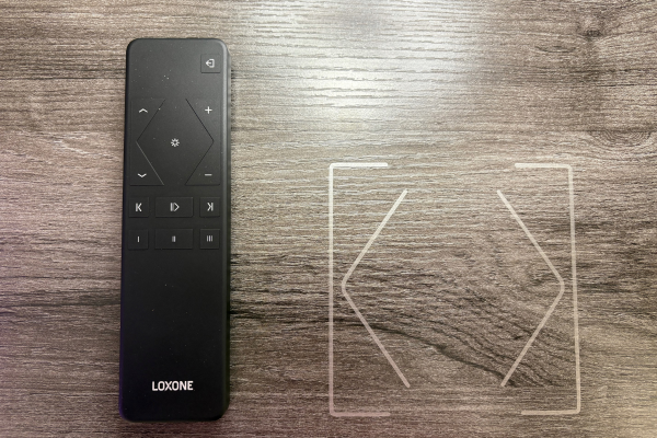 Loxone Remote Air handheld controller next to Loxone Touch Surface Tree outline on dark wood desk surface