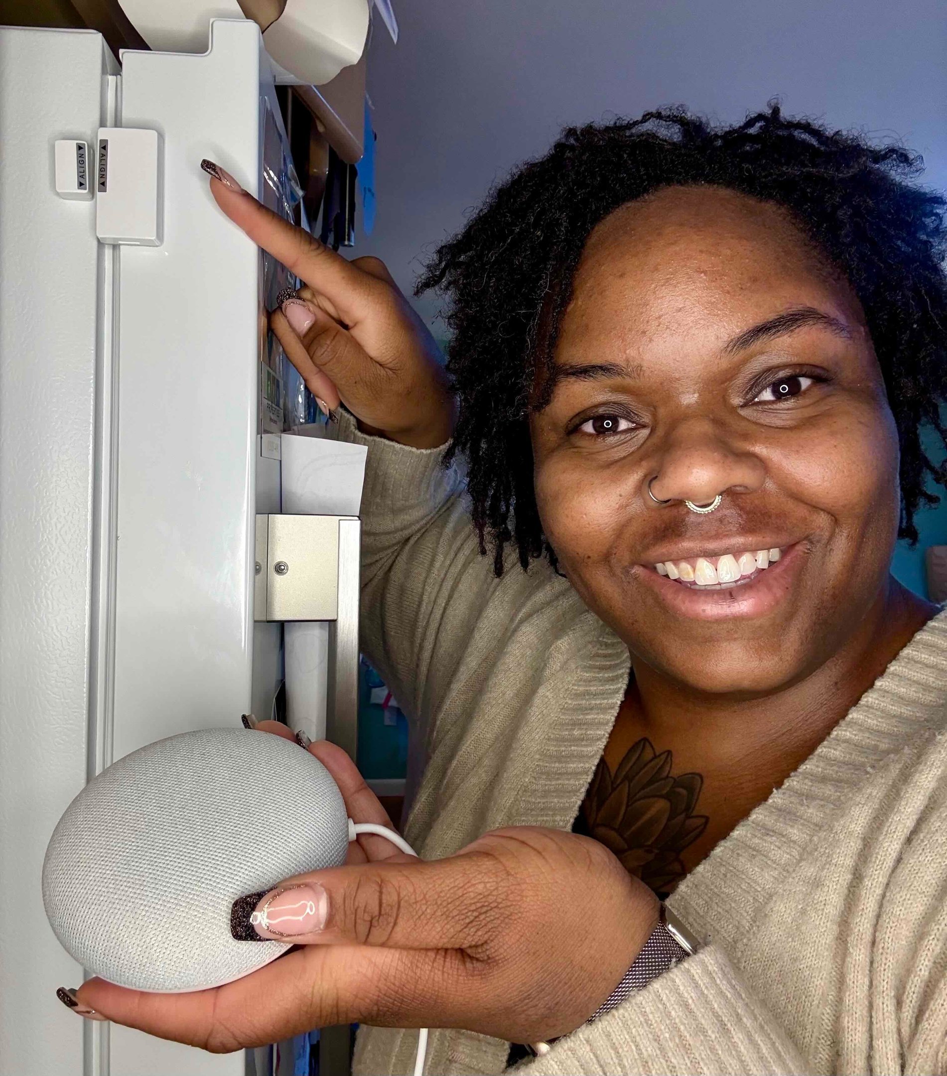 Image of Ashley pointing at a smart contact sensor affixed to a fridge and holding a smart speaker