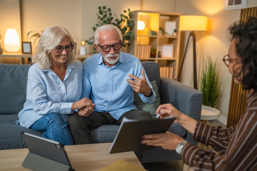 Older couple reviewing a home safety assessment report on a tablet with a consultant in their living room