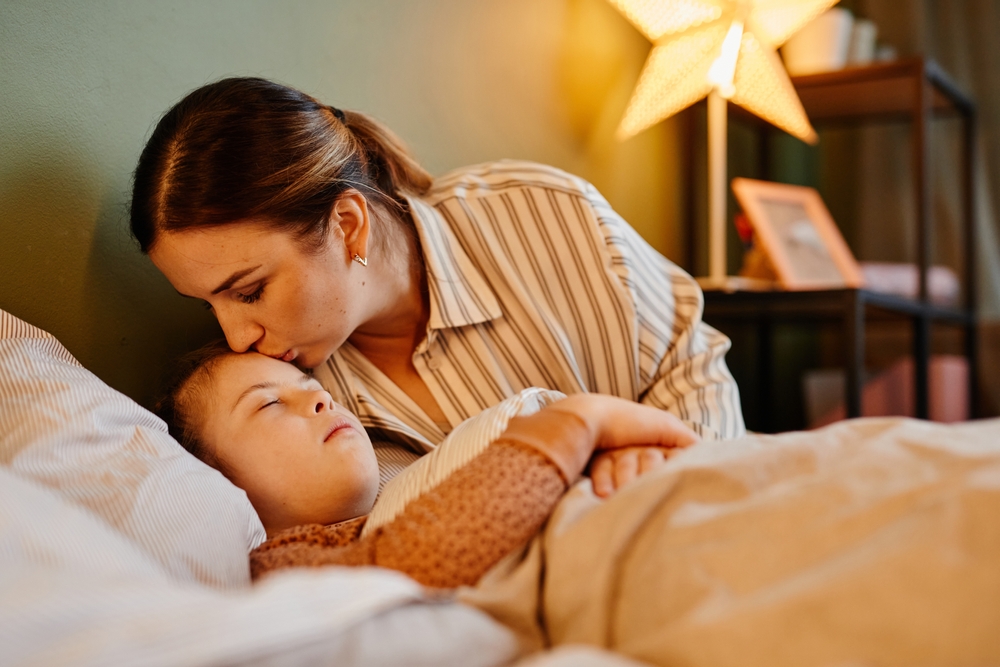 mother kissing sleeping child on forehead in dimly-lit bedroom scene