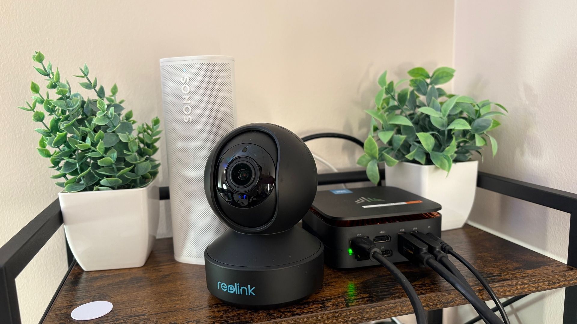 Image of reolink camera, mini pc set in front of a sonos speaker and plants
