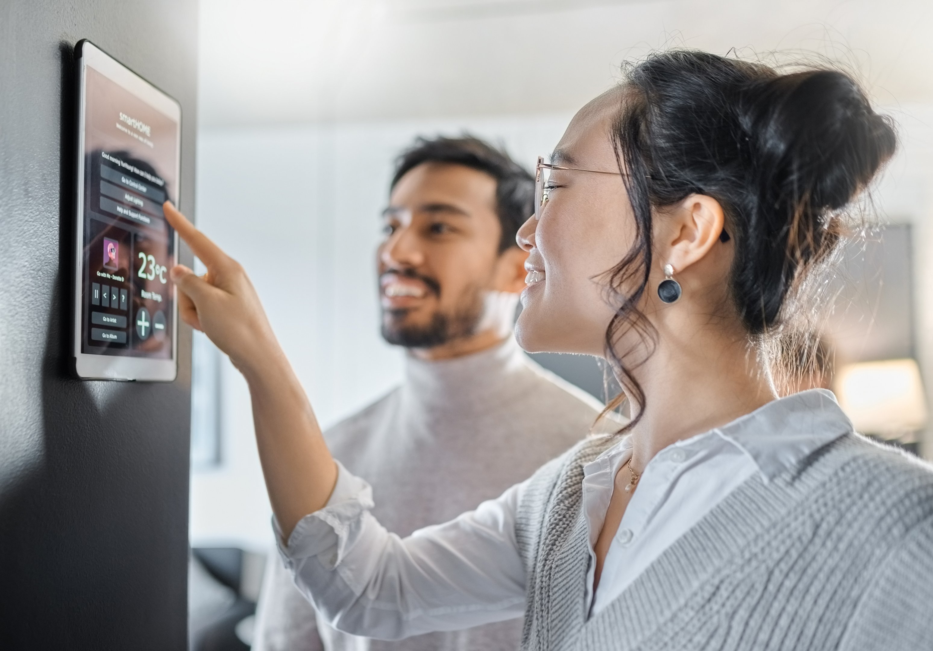man and woman adjusting settings on wall-mounted smart home tablet